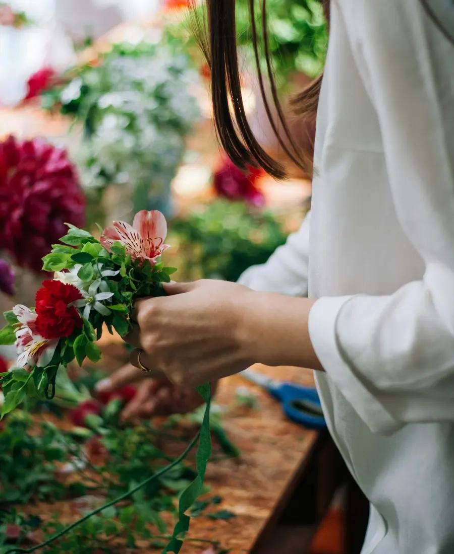 A florist's hands wrapping a small bouquet of alstroemeria and red carnations at a wooden workbench